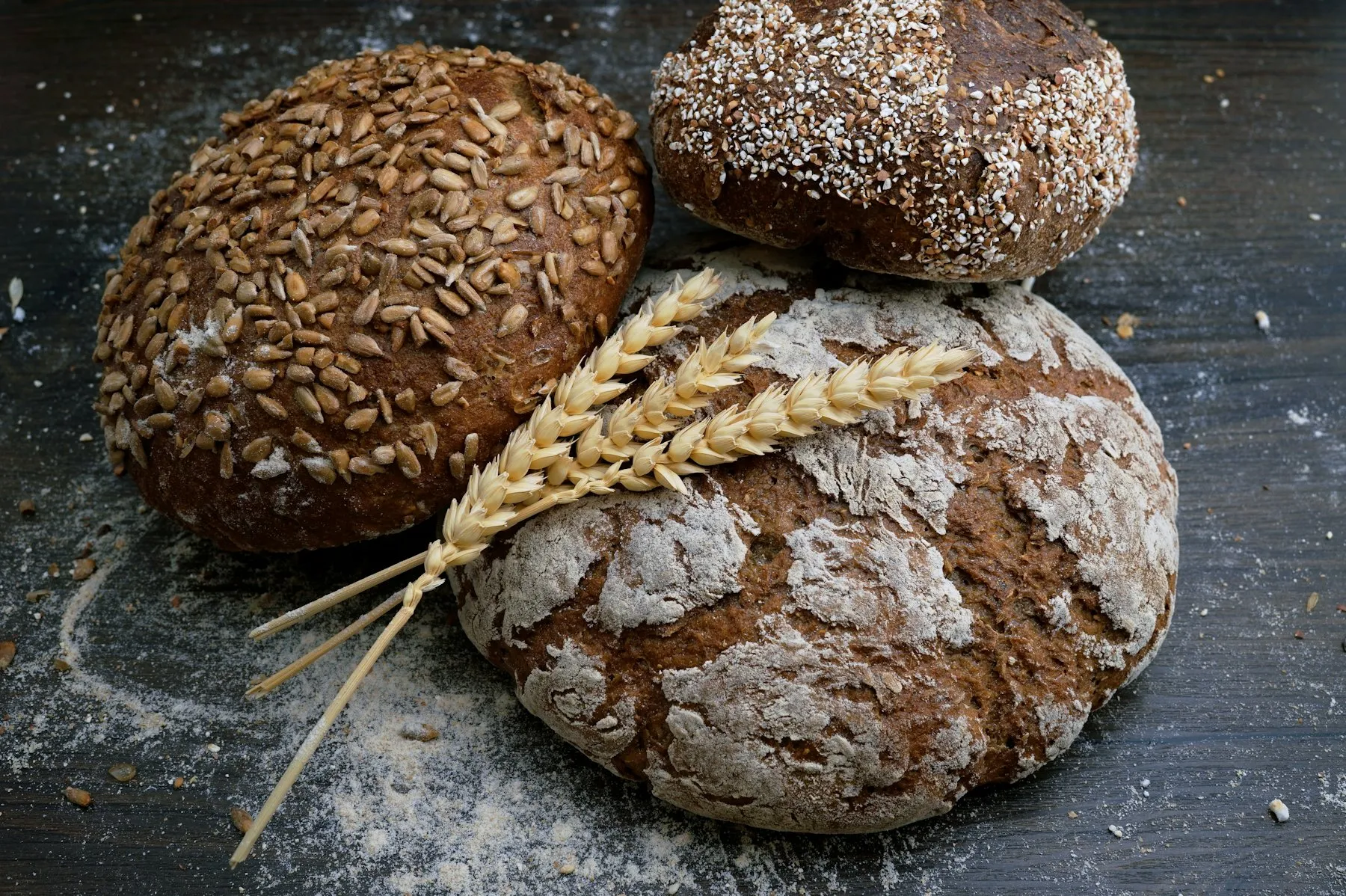 Rustic artisan loaves dusted with flour and topped with seeds, with a stalk of wheat
