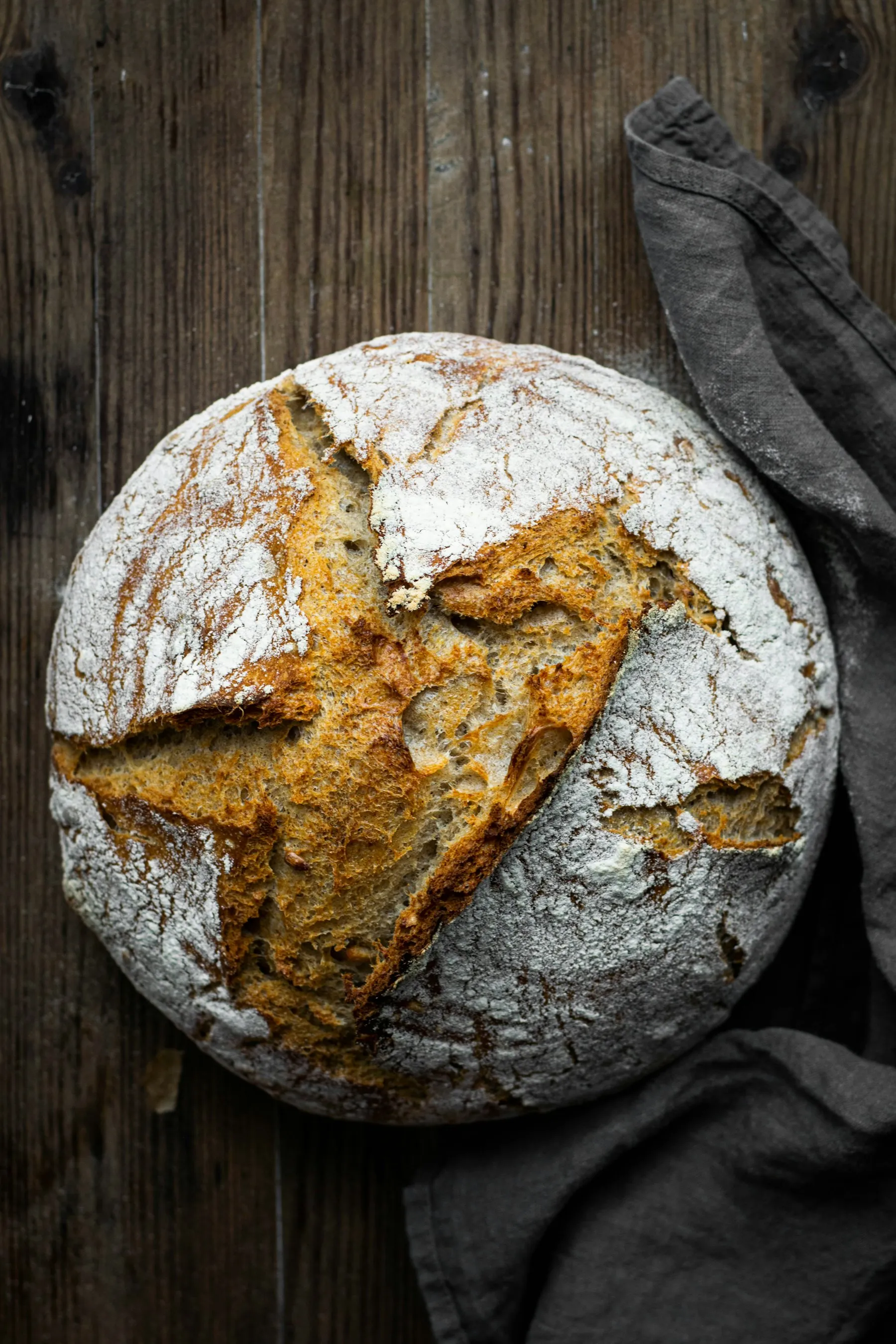 Crusty scored sourdough boule on a dark wooden board
